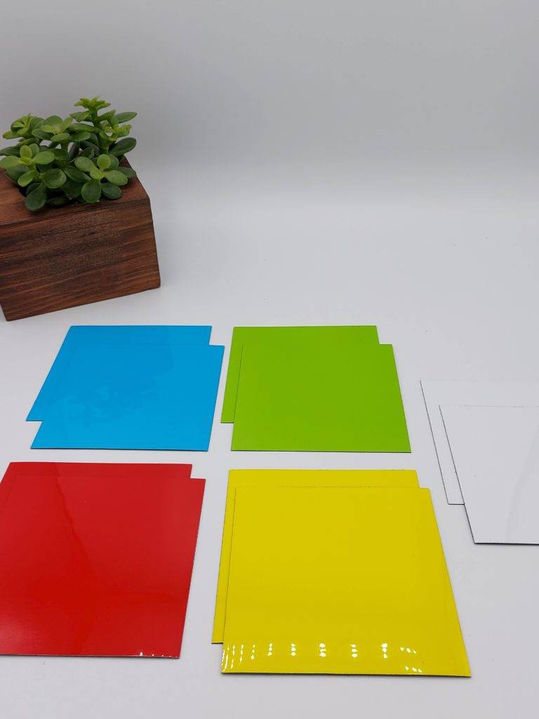 Bunte Magnete (quadratisch) in verschiedenen Farben mit einer Pflanze im Hintergrund (größerer Ausschnitt).