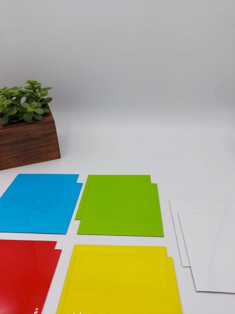 Bunte Magnete (quadratisch) in verschiedenen Farben mit einer Pflanze im Hintergrund.